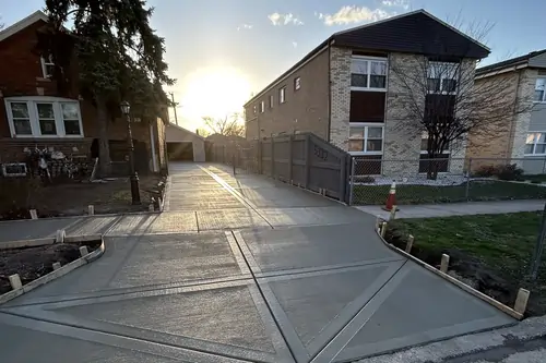 Newly poured concrete driveway with geometric patterns, flanked by a residential building and a tree at sunset